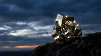Golden pyrite mineral crystal formation on rocky surface against dramatic stormy sky at sunset for geology education and natural science materials.