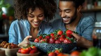 Happy African American couple enjoying fresh strawberries together in modern kitchen, healthy eating lifestyle and romantic cooking moments at home.