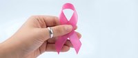 Hand holding pink ribbon symbol for breast cancer awareness campaign and women health support on white background.