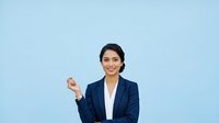 Young South Asian woman in professional navy blazer and white shirt smiling while pointing, isolated on light blue background for corporate and business design projects.