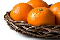 Fresh ripe oranges with textured peel in rustic woven basket against white background, macro food photography with selective focus and natural lighting.