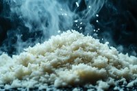Steaming white rice grains in dramatic lighting with rising smoke and steam against dark background, macro food photography showing texture and detail of cooked rice.