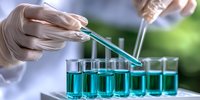 Laboratory scientist in protective gloves conducting research with blue liquid samples in test tubes, performing chemical analysis in modern facility.