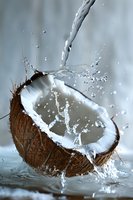 Fresh water pouring into halved coconut creating dynamic splash against soft gray background, showcasing natural tropical refreshment.