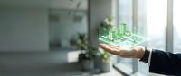 Businessman holding holographic green cityscape with buildings and trees in palm, representing sustainable urban development and smart city technology in modern office environment.