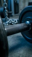 Close-up of heavy barbell weights with textured grip handle and chain, ready for strength training and fitness workouts in gym environment.