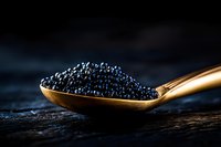 Black caviar in golden spoon on dark wooden surface with dramatic lighting for luxury gourmet food presentation and culinary advertising.