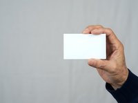 Male hand holding blank white business card against neutral gray background for corporate branding and marketing purposes.