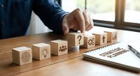 Business professional arranging wooden blocks with strategy icons on desk near window for corporate planning and development concepts.