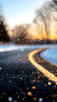 Snowy winter road with glowing yellow lane markings at sunset, bokeh lights and falling snowflakes creating festive seasonal atmosphere for holiday and travel concepts.