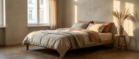 Cozy modern bedroom interior with warm beige tones, natural lighting, wooden bed frame and decorative pampas grass creating peaceful sleeping space.