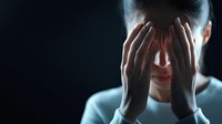 Asian woman covering face with hands in dark room, dramatic lighting emphasizes emotional distress and vulnerability. Mental health concept for anxiety and depression.