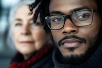 Young African American man with glasses and beard in focus with blurred woman in background, representing diversity and connection in modern relationships.