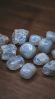 Collection of polished moonstone gems with blue flash adularescence scattered on rustic wooden surface for jewelry making and crystal healing practices.