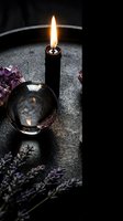 Black candle burning with crystal ball and lavender flowers on dark stone surface creating mystical atmospheric mood for spiritual practices.
