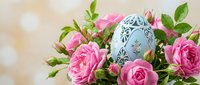 Decorative Easter egg with intricate patterns nestled among fresh pink roses and green foliage for spring holiday celebrations and seasonal decor.