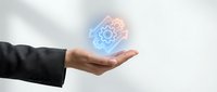 Hand of a professional in dark business attire holding a glowing digital gear icon with blue and orange light effects, representing technology, innovation, and engineering solutions.