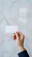 Hand holding blank white card against marble background, ideal for business card mockups, branding presentations, and corporate identity designs.