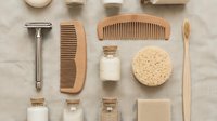 Eco-friendly men's grooming kit with wooden combs, bamboo toothbrush, safety razor, natural sponge and glass bottles on beige linen background.