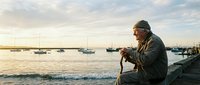 Elderly fisherman with weathered hands holding rope at peaceful harbor during golden hour sunset with sailboats anchored in calm waters and wooden dock.