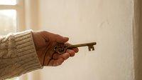 Hand holding vintage ornate bronze key in warm sunlight by window, symbolizing opportunity, access, success, and new beginnings in cozy home setting.