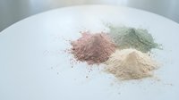Colorful cosmetic clay powder piles in pink green and beige on white surface for natural skincare beauty treatments and spa wellness applications.