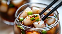 Asian fish ball soup with vegetables in clear broth served in glass bowl with black chopsticks, traditional comfort food for restaurant menu design.