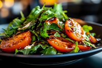 Fresh mixed greens salad with sliced tomatoes and herbs on dark plate, healthy vegetarian meal for restaurant menu and food photography.