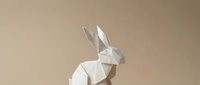 Geometric white paper rabbit sculpture with angular facets on a neutral beige background, minimalist origami art for Easter and modern decor.