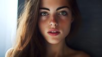 Young attractive Caucasian woman with long brown hair and natural makeup looking directly at camera with soft lighting for beauty and lifestyle content.