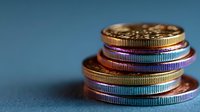 Stack of colorful metallic coins with rainbow iridescent finish on blue background for financial concepts and cryptocurrency designs.
