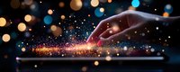 Female hand touching digital tablet screen with magical light sparkles and glowing particles creating trail effect against dark background with bokeh lights.