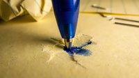 Ballpoint pen with blue ink writing on beige paper, close-up of nib touching surface during writing process for stationery and office supplies.