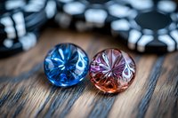 Sparkling blue and pink crystal gems with starburst cut pattern on rustic wooden surface, poker chips in background. Macro jewelry photography.
