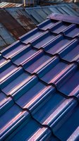 Close-up of blue ceramic roof tiles with metallic sheen and weathered patina, showing overlapping rows and textured surface details. Use for roofing, construction, architecture, and home improvement projects.