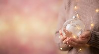 Woman in cozy sweater holding glowing glass globe ornament with warm bokeh lights creating magical holiday atmosphere for seasonal celebrations.