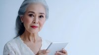 Elegant senior Asian woman with gray hair using digital tablet, mature female browsing internet technology for modern lifestyle and communication.