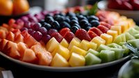 Fresh colorful fruit platter arranged in rainbow pattern with strawberries, blueberries, pineapple, melon, and grapes. Healthy eating and party catering concept.
