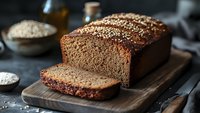 Freshly baked homemade whole grain bread with sesame seeds on wooden cutting board, sliced and ready to serve on dark background.
