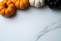 Decorative orange, white and black mini pumpkins arranged on marble background creating seasonal border with copy space for autumn holiday designs.