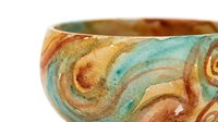 Decorative ceramic bowl with swirling patterns in warm earth tones and turquoise, featuring hand-painted ornamental designs suitable for home decor and tableware styling.
