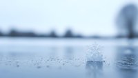 Delicate ice crystal formation on frozen lake surface with soft winter landscape background creating serene cold weather atmosphere for seasonal content.