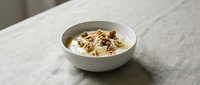 Creamy yogurt bowl topped with crunchy walnuts and golden honey, served in a white ceramic bowl on a linen tablecloth.