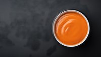 Orange creamy sauce in white ceramic bowl on dark background, top view. Food photography with copy space for menu or recipe design.