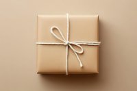 Kraft paper gift box wrapped with white twine bow on neutral beige background, overhead view for holiday, birthday, and special occasion packaging design.