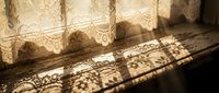 Delicate lace curtains casting intricate shadow patterns on wooden floor in warm sunlight creating romantic vintage home interior atmosphere.