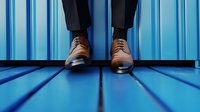 Elegant brown leather oxford shoes on male feet against vibrant blue industrial background, creating striking contrast and modern business perspective.
