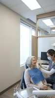 Female dentist examining senior Caucasian woman patient in modern dental office with natural lighting and contemporary equipment for oral healthcare consultation.