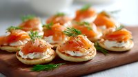 Mini blini pancakes topped with smoked salmon, cream cheese and fresh dill garnish served on wooden cutting board, elegant appetizer for catering and events.