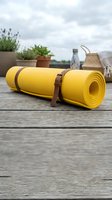 Yellow yoga mat with leather strap on wooden deck with plants and water bottle in background for fitness and wellness lifestyle.